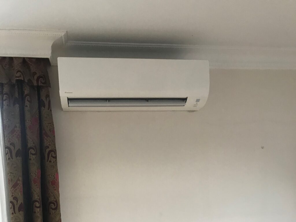 Nástěnná klimatizace Daikin instalovaná nad oknem vedle závěsu