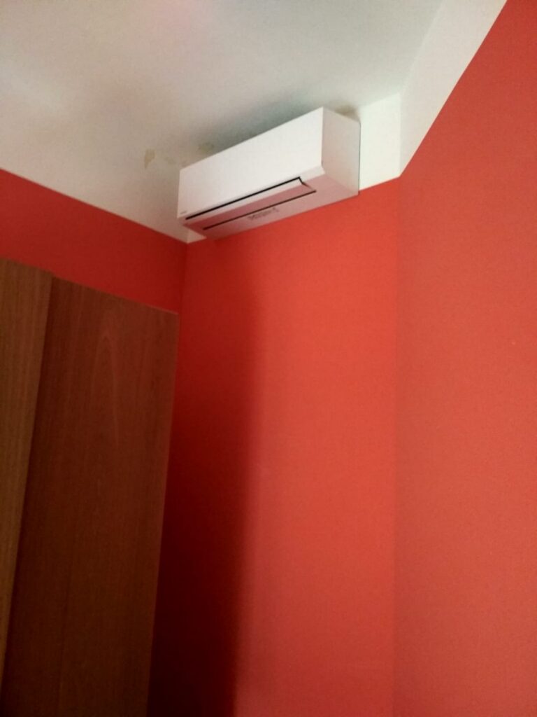 Bílá nástěnná klimatizace pod stropem v místnosti s červenými stěnami