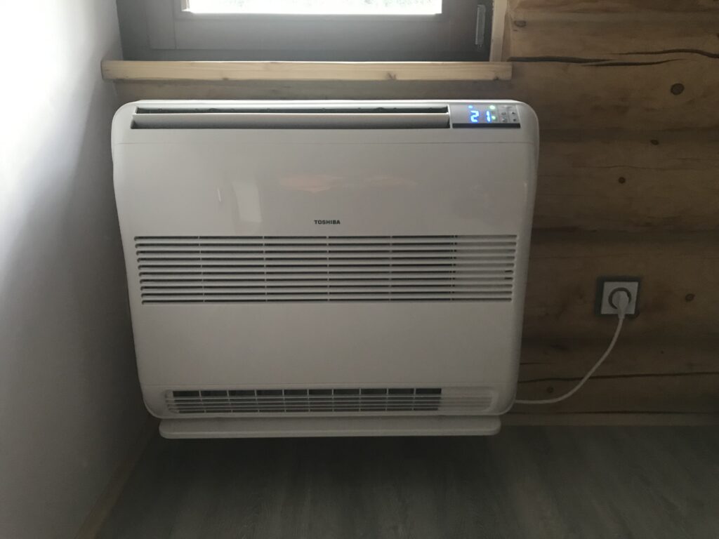 Bílá parapetní klimatizace Toshiba pod oknem v interiéru